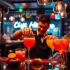 Experience the excitement of a cocktail kurs berlin with a skilled bartender mixing vibrant cocktails in a lively bar.